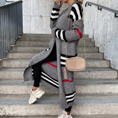 Frau in grauem gestreiftem Strickmantel, schwarze Leggings, weiße Sneaker, beige Umhängetasche.