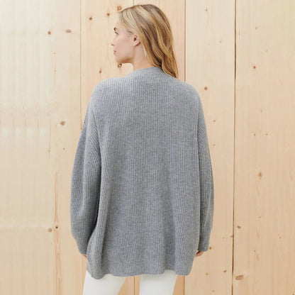 Frau in grauem Strickpullover aus Wolle, Rückansicht, vor Holzwand.