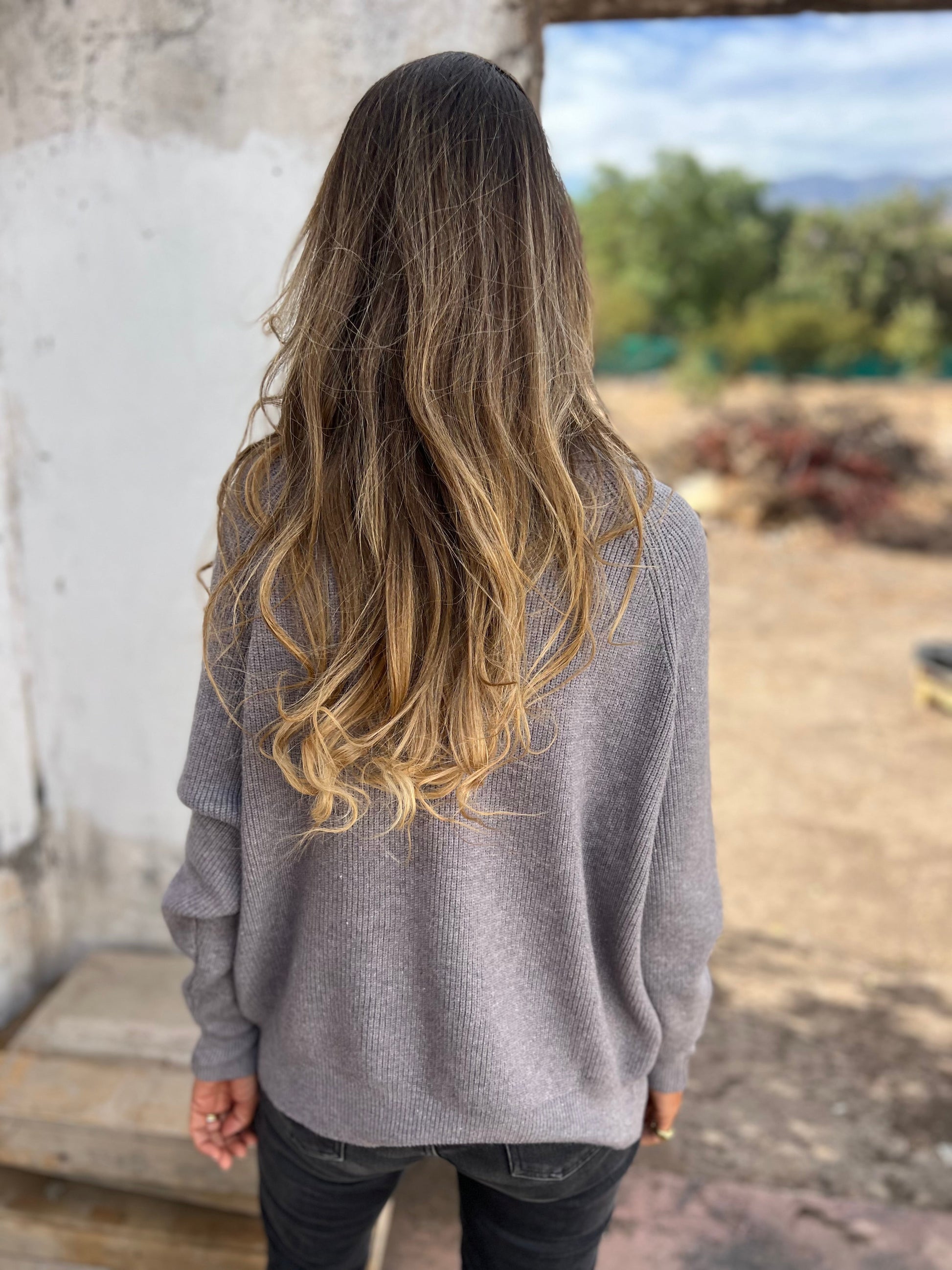 Frau in grauem V-Ausschnitt-Pullover, lange Ärmel, draußen, Rückansicht.
