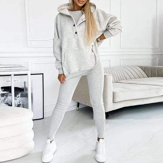 Frau in grauem Kapuzenpullover und Leggings, gemütliches Lounge-Set, modernes Wohnzimmer.
