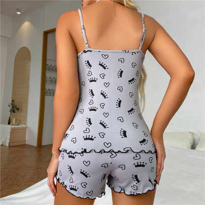 Frau in grauem Pyjama-Set mit Kronen- und Herzmuster, Schlafzimmer-Hintergrund.
