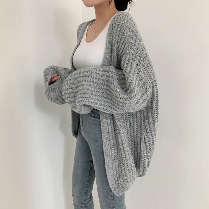 Grauer Damen-Strickcardigan, gemütlich und stilvoll, über weißem Top und Jeans getragen.