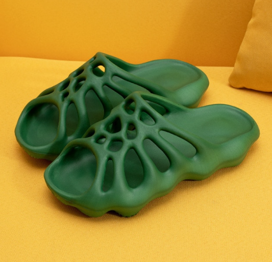 Grüne, futuristische Sandalen aus Kunststoff auf gelbem Hintergrund, modisch und bequem.