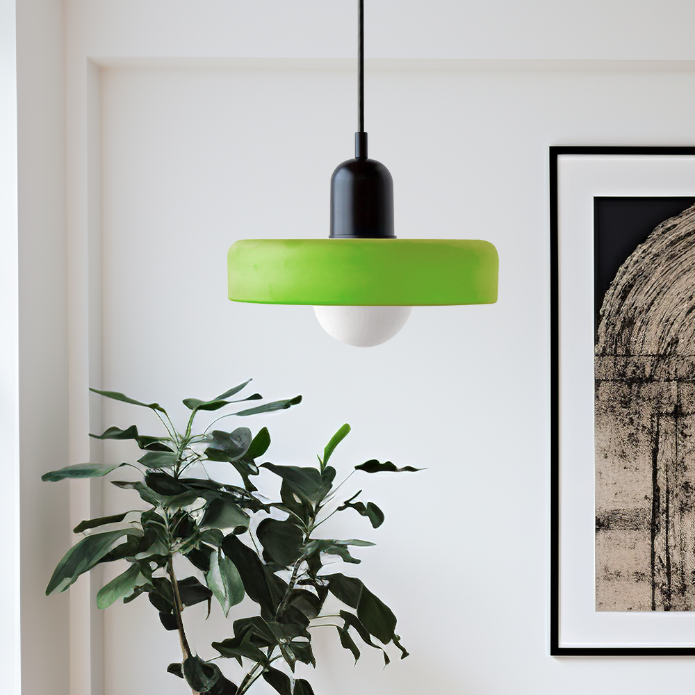 Grüne Hängelampe aus Glas, modernes Design, über Zimmerpflanze und Kunstwerk an weißer Wand.
