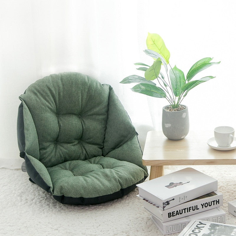 Grüner, verstellbarer Bodensessel aus Stoff neben Holztisch mit Pflanze und Büchern im Wohnzimmer.