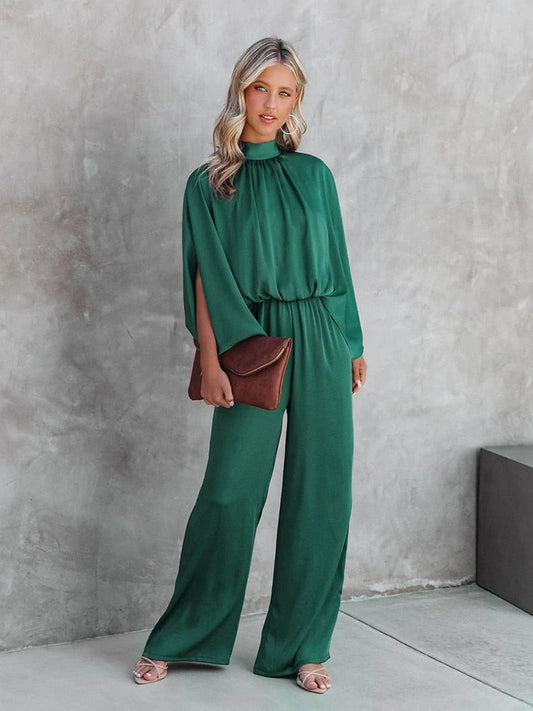 Frau im grünen Jumpsuit mit brauner Clutch vor grauer Wand, elegante Mode, Abendgarderobe.