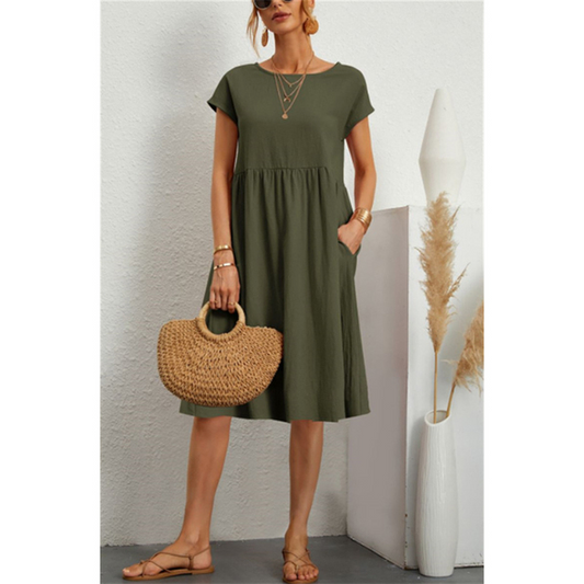 Frau in olivgrünem Baumwoll-Leinen-Kleid, Boho-Stil, mit Strohtasche und Sandalen.
