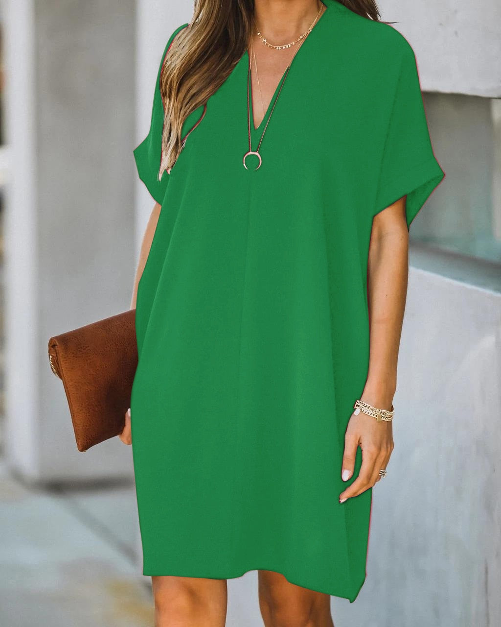 Frau in grünem Sommerkleid mit V-Ausschnitt, brauner Clutch, lässiger Stil, modisch.