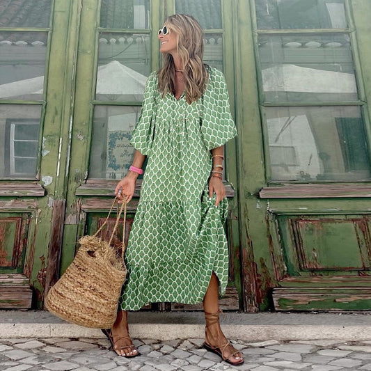 Frau in grünem Maxikleid mit geometrischem Muster, Strohtasche, Sandalen, vor grüner Holztür.