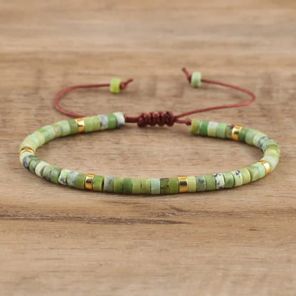 Grünes Perlenarmband mit goldenen Akzenten, verstellbar, handgefertigt, auf Holzoberfläche.
