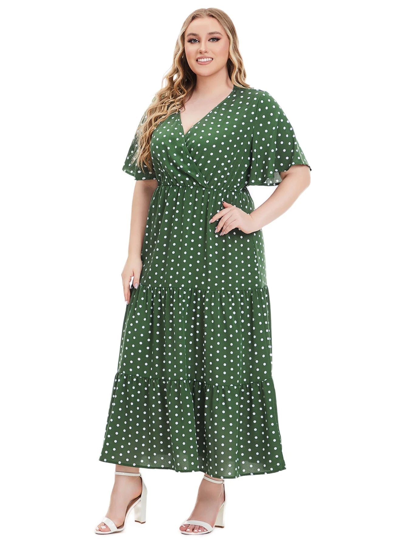 Frau im grünen gepunkteten Maxikleid, Plus-Size, lächelnd, weiße Sandalen.