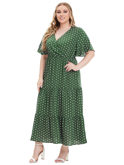 Frau im grünen gepunkteten Maxikleid, Plus-Size, lächelnd, weiße Sandalen.