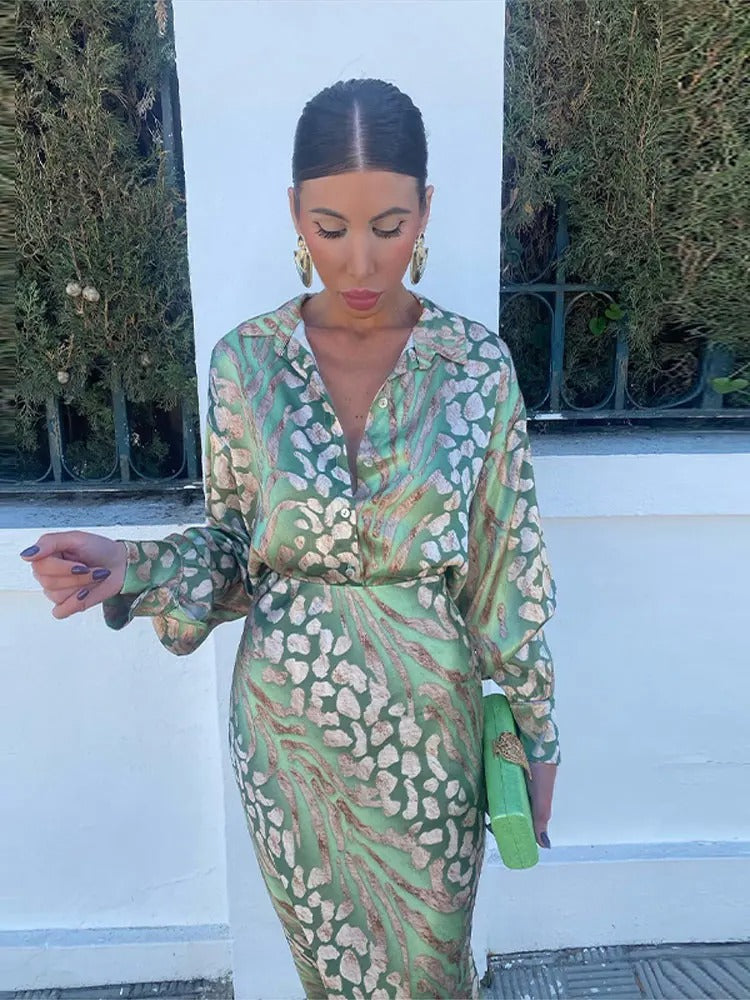 Frau in grünem Seidenkleid mit Muster, hält grüne Clutch, elegante Mode, draußen.