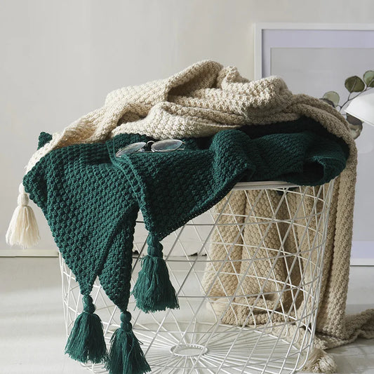 Grüner Strickplaid mit Quasten auf weißem Drahtkorb, dekorativer Wohnaccessoire.