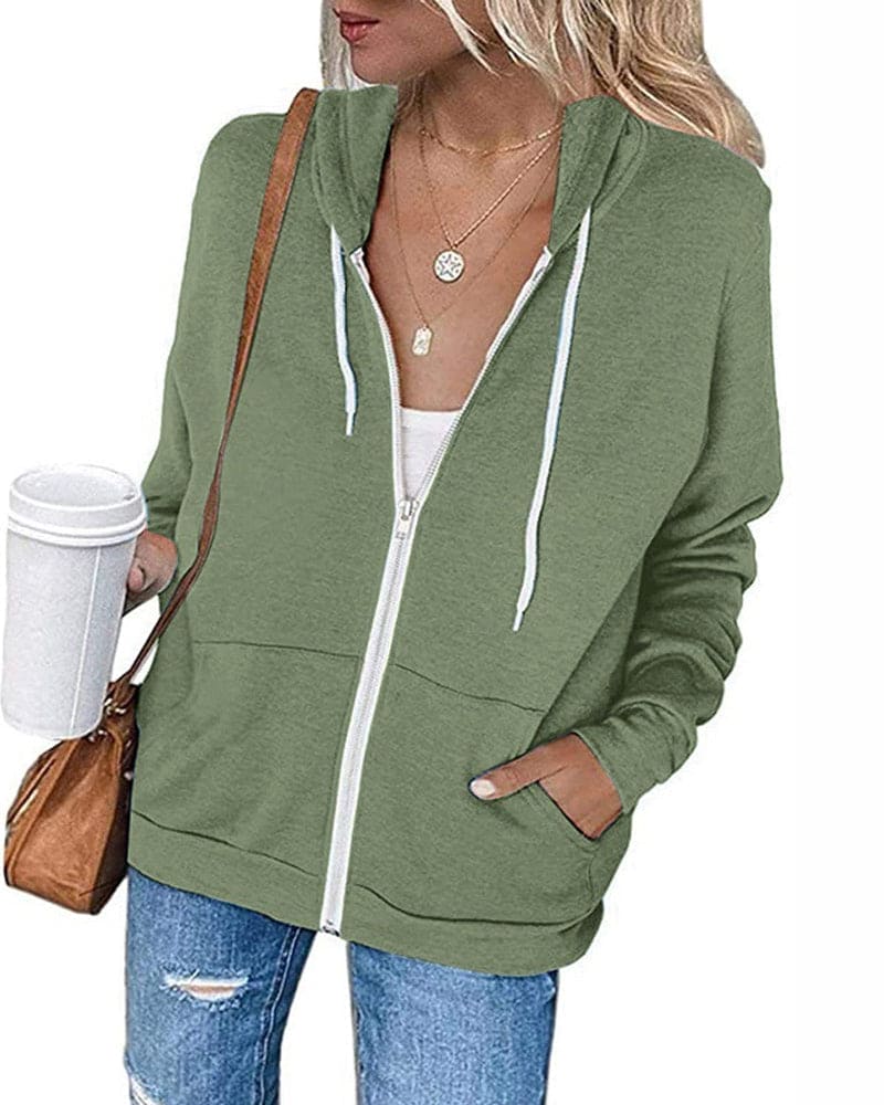 Frau in grüner Kapuzenjacke mit Reißverschluss, Kaffeebecher, braune Tasche, lässiger Stil.