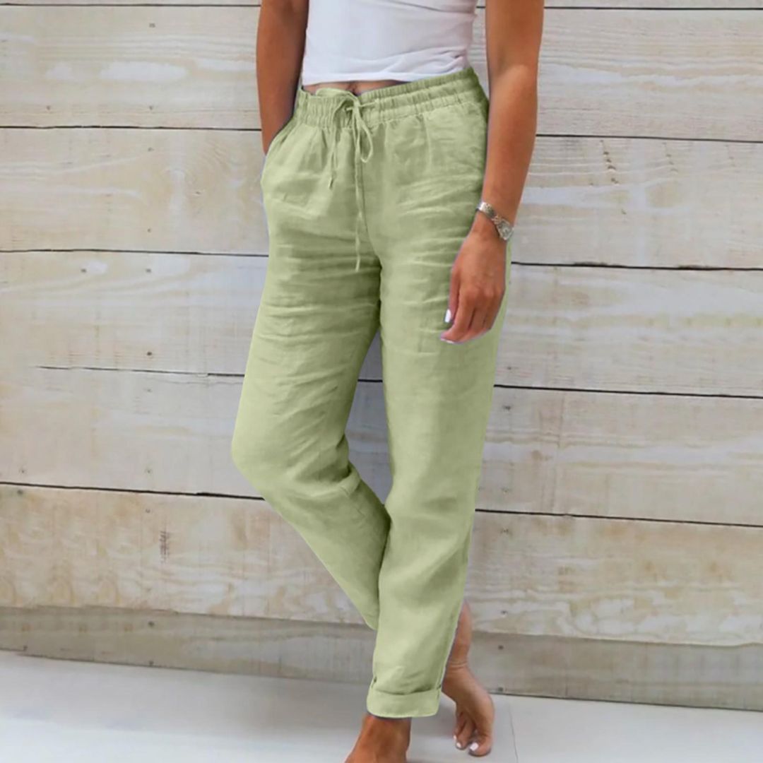 Frau in grüner Leinenhose, weißes Top, Holz-Hintergrund, lässige Sommermode.