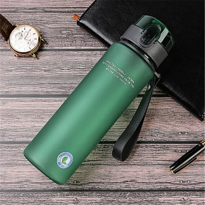 Grüne Edelstahl-Wasserflasche mit Trageschlaufe auf Holztisch, ideal für Outdoor-Aktivitäten.