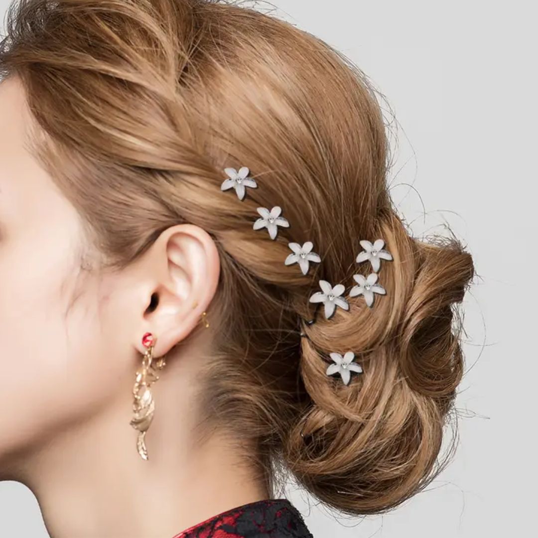 Frau mit braunem Haar, verziert mit weißen Blumen-Haarnadeln, eleganter Look, goldene Ohrringe.
