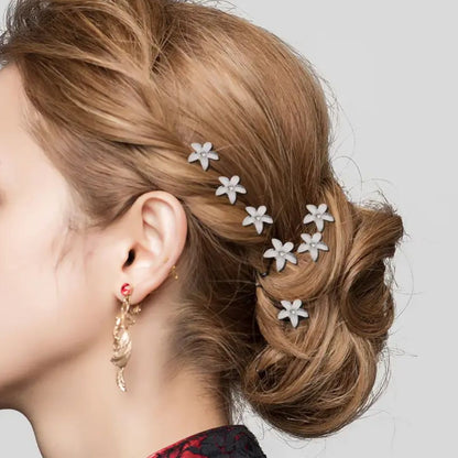 Frau mit braunem Haar, verziert mit weißen Blumen-Haarnadeln, eleganter Look, goldene Ohrringe.