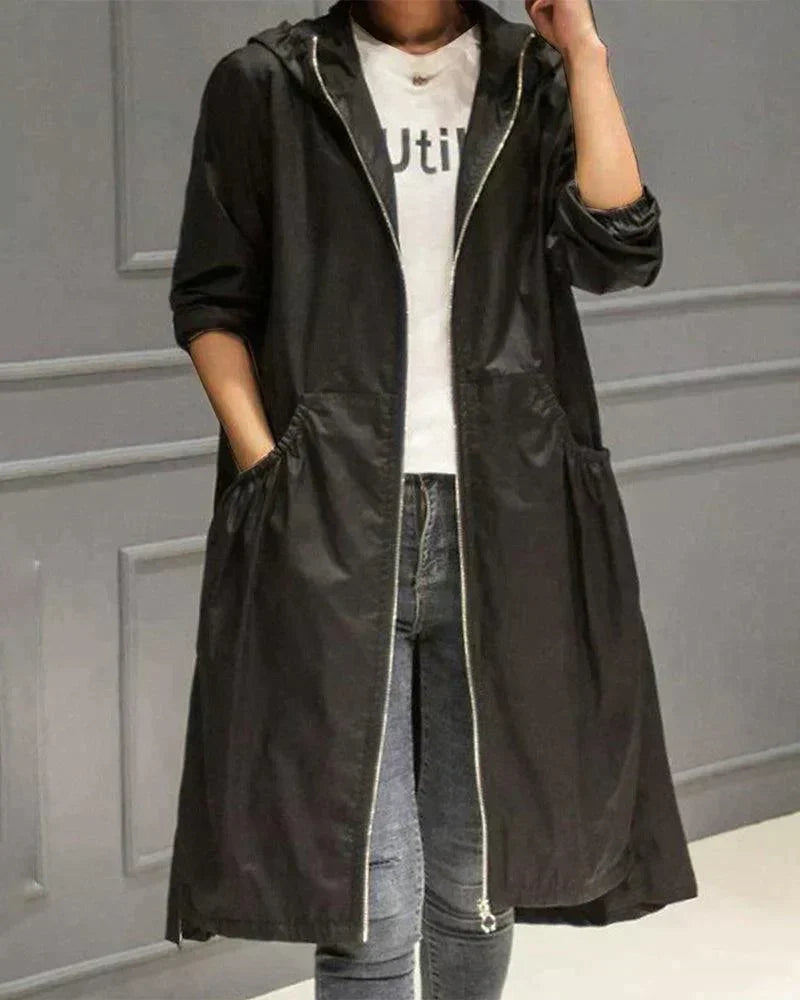 Schwarzer Regenmantel mit Kapuze und hellem Reißverschluss, getragen mit Jeans, eine Hand in der Tasche, eine am Kragen 4