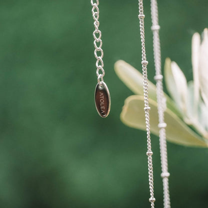 Silberkette mit graviertem ATOLEA-Anhänger, elegantes Schmuckdesign vor grünem Hintergrund.