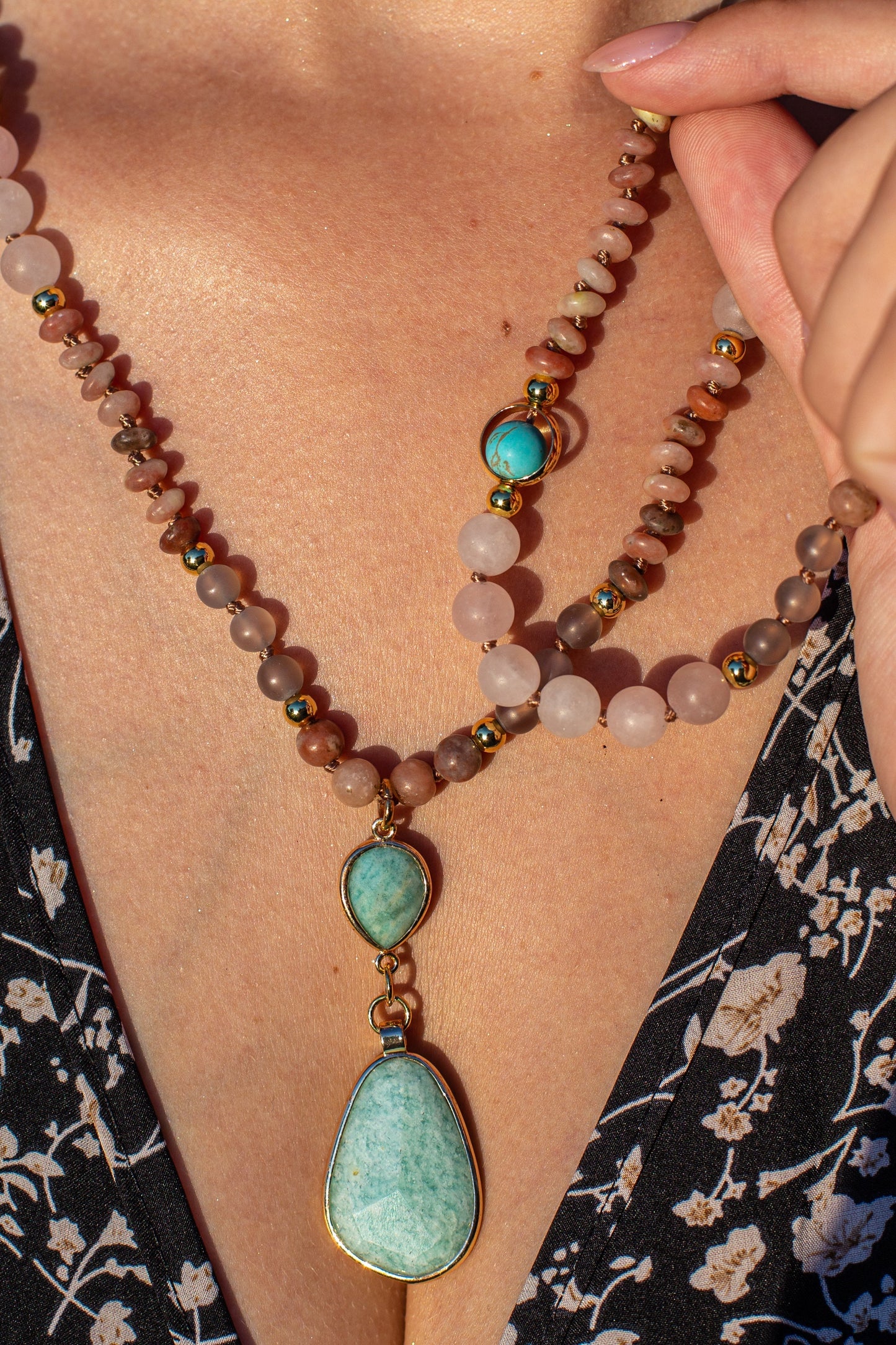 Frau mit Halskette aus Rosenquarz und türkisfarbenem Anhänger, eleganter Schmuck, Nahaufnahme.