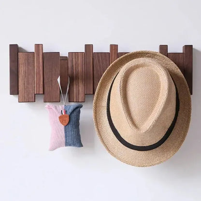 Dunkle Holzleiste an weißer Wand, an den Haken hängen ein Strohhut und ein rosa-blaues Stoffsäckchen 2