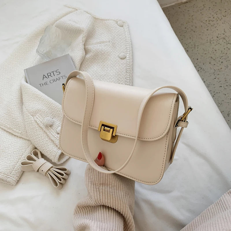 Beige Lederhandtasche mit goldener Schnalle auf weißem Bett, modisch, elegant, Damenaccessoire.