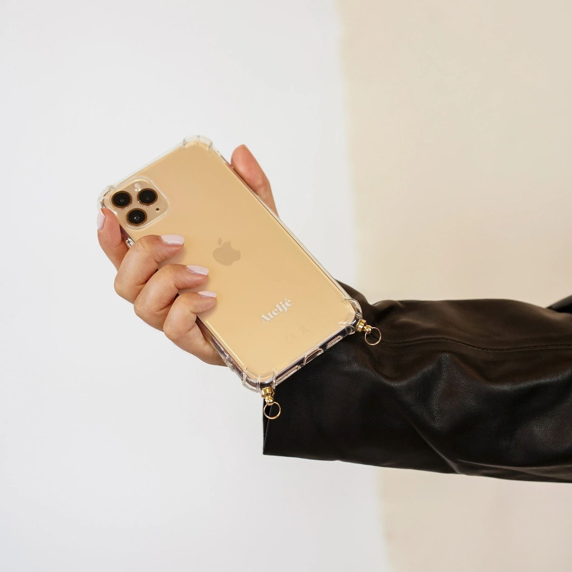 Hand hält iPhone 11 Pro in transparenter Handyhülle mit goldenen Details, schwarzer Lederjacke.