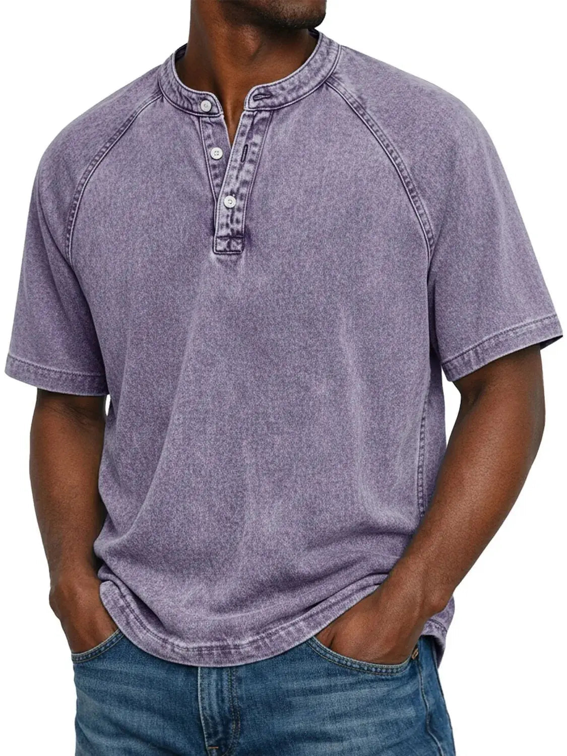 Mann trägt das ausgewaschene Henley-Shirt mit Raglanärmeln in Flieder, Hände in den Jeanstaschen, Knopfleiste vorne. 1