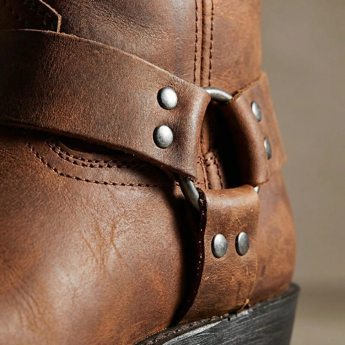 Nahaufnahme des Riemens mit metallenem Ring und Nieten sowie der feinen Lederstruktur am braunen Stiefel. 3
