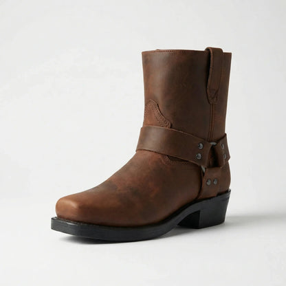 Brauner Stiefel mit dekorativem Riemen und eckiger Spitze, seitlich schräg von vorne vor hellem Hintergrund fotografiert. 4
