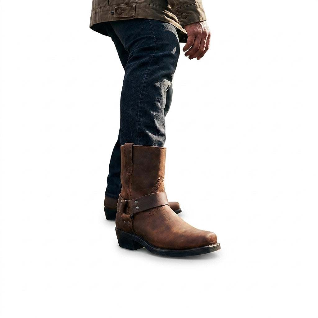 Mann in dunkler Jeans und olivgrüner Jacke trägt den braunen Lederstiefel mit Riemen und Nieten im seitlichen Gehen. 1