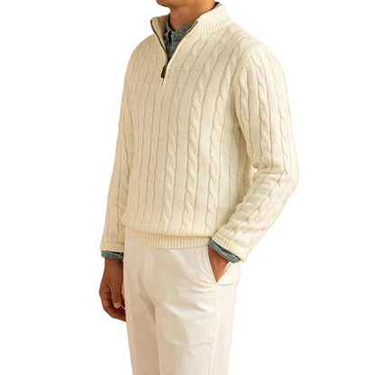 Mann trägt den cremeweißen Zopfstrick-Pullover mit offenem Reißverschluss über einem Jeanshemd, dazu helle Hose, seitlich fotografiert. 1