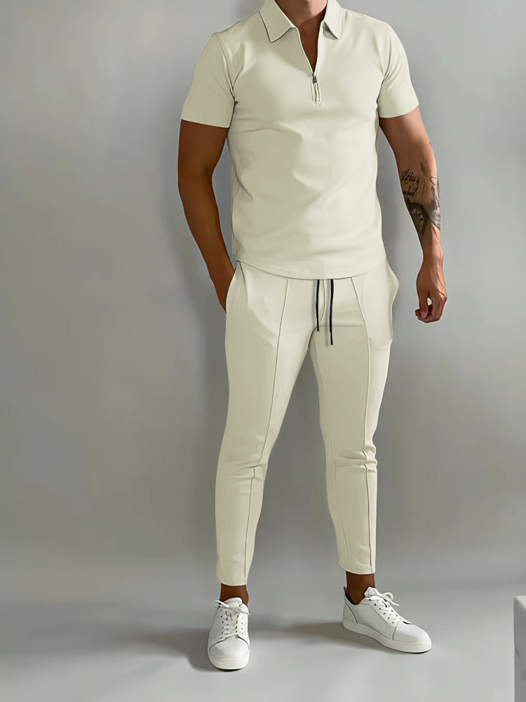 Mann in cremefarbenem Poloshirt und Jogginghose, sportlich-eleganter Look, weiße Sneaker.