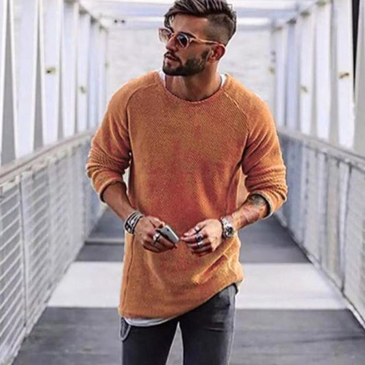 Mann mit orangefarbenem Pullover, Sonnenbrille und Jeans auf Brücke, modischer Freizeitlook.