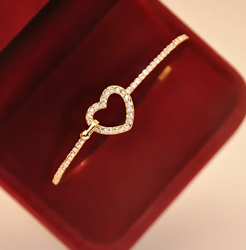 Goldenes Armband mit Herzanhänger und Diamanten in roter Schmuckschatulle, elegantes Design.