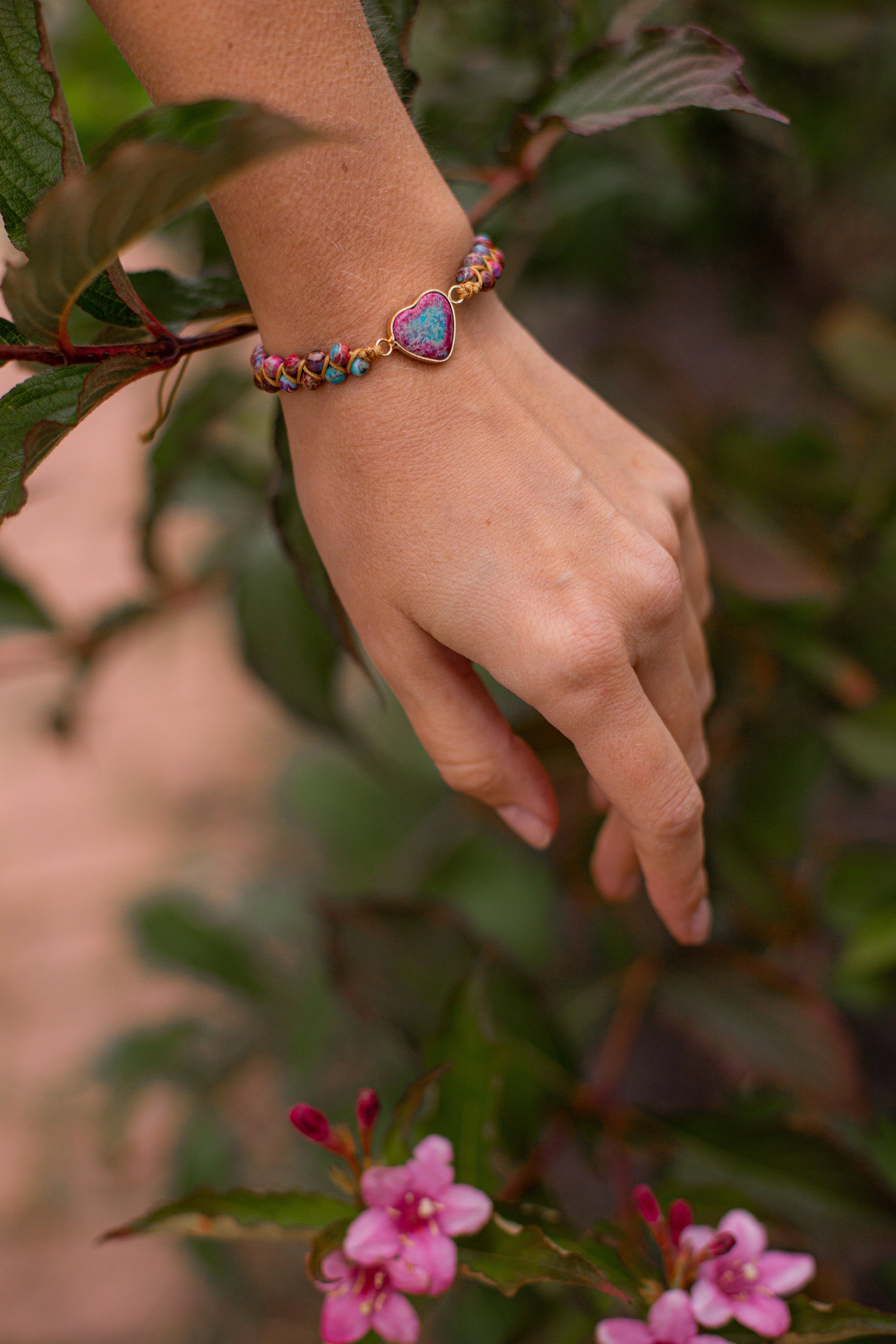 Hand mit Herz-Armband aus bunten Perlen, Naturhintergrund, Schmuck, Modeaccessoire.