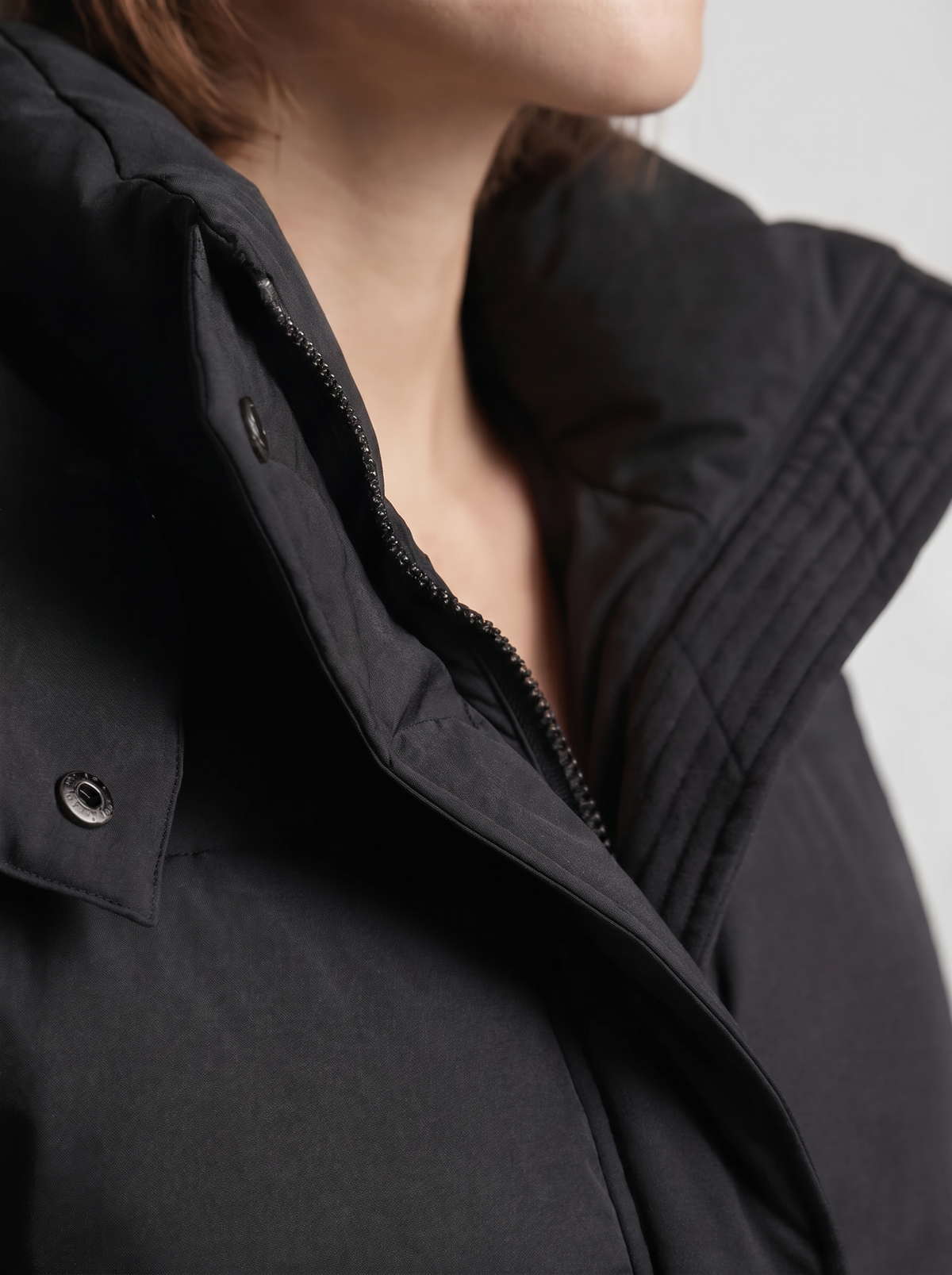 Detailaufnahme von Stehkragen, Reißverschluss und Druckknopf der schwarzen Steppjacke, am Model 7