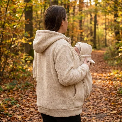 Seitenansicht einer Frau im beigen Sherpa-Hoodie, die ihr Baby im Trageeinsatz hält, auf einem Waldweg im Herbst. 6