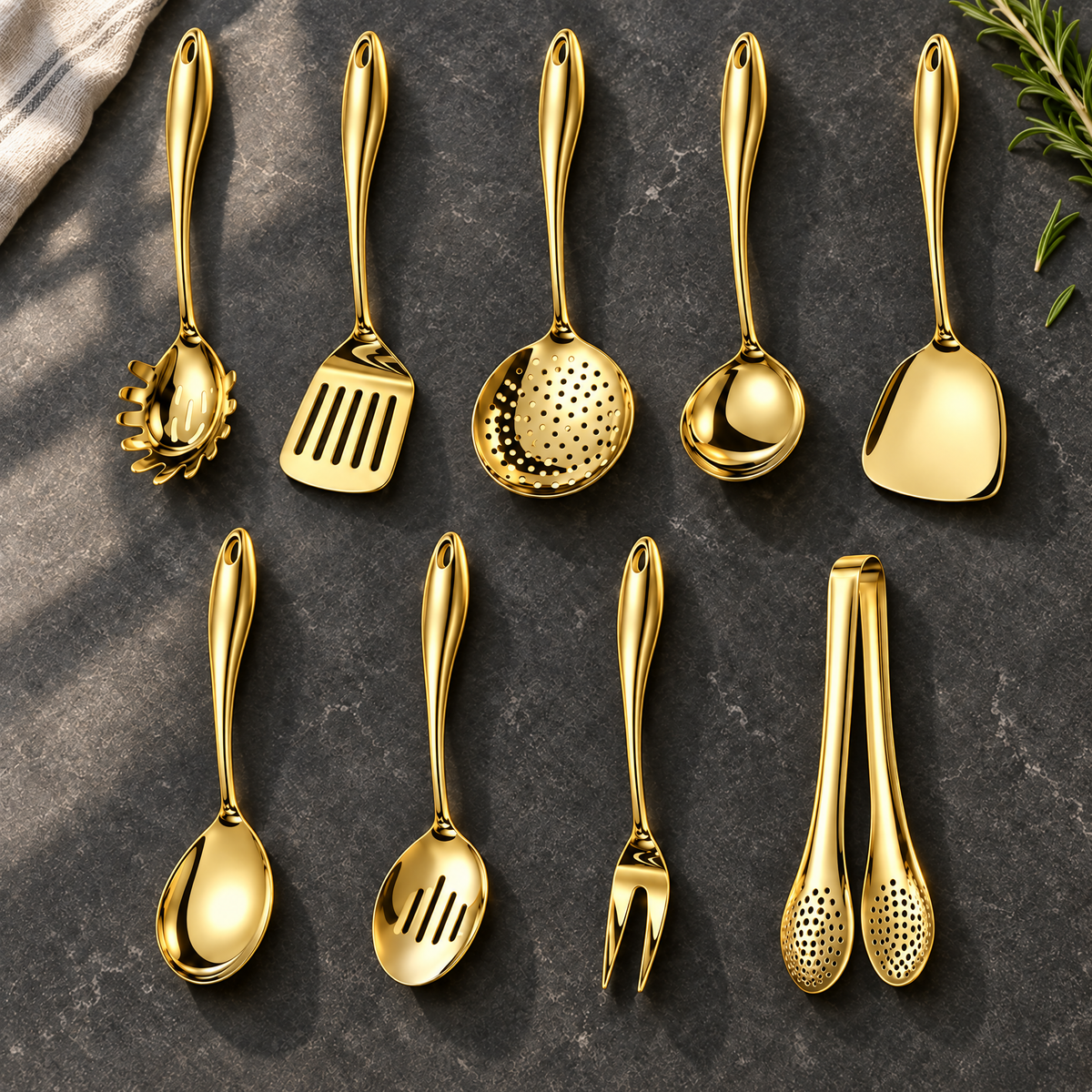 Neunteiliges goldfarbenes Set in zwei Reihen auf dunklem Stein, mit Sieblöffel, Gabel, Zange und Wendern, daneben Rosmarinzweig und helles Tuch. 25