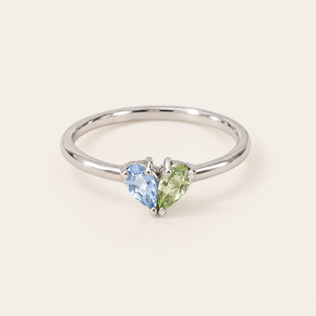 Silberfarbener Ring in Frontalansicht mit einem hellblauen und einem grünen tropfenförmigen Stein, die zusammen ein Herz formen. 5