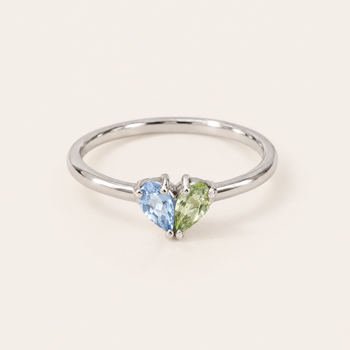 Silberfarbener Ring in Frontalansicht mit einem hellblauen und einem grünen tropfenförmigen Stein, die zusammen ein Herz formen. 5