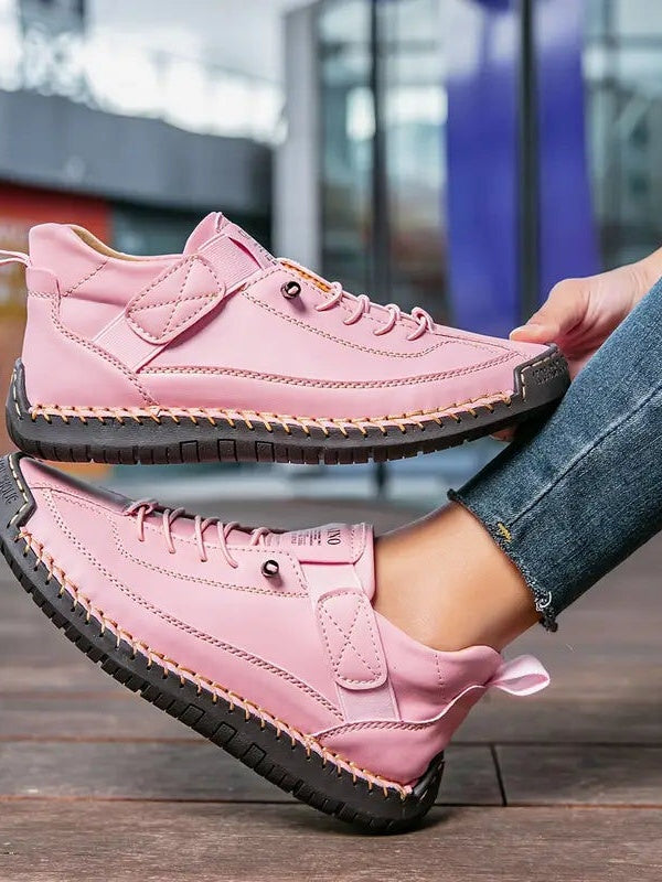 Rosa Sneaker mit dunkler Sohle, von einer Frau seitlich gehalten, Blick auf Riemen und Schnürung 13