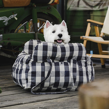 Weißer Hund in kariertem Hundebett auf Holzterrasse, gemütlich und stilvoll.