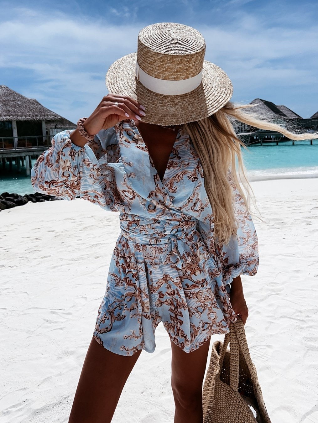 Frau im blauen Sommerkleid mit Strohhut am Strand, Urlaubsmode, tropische Kulisse.