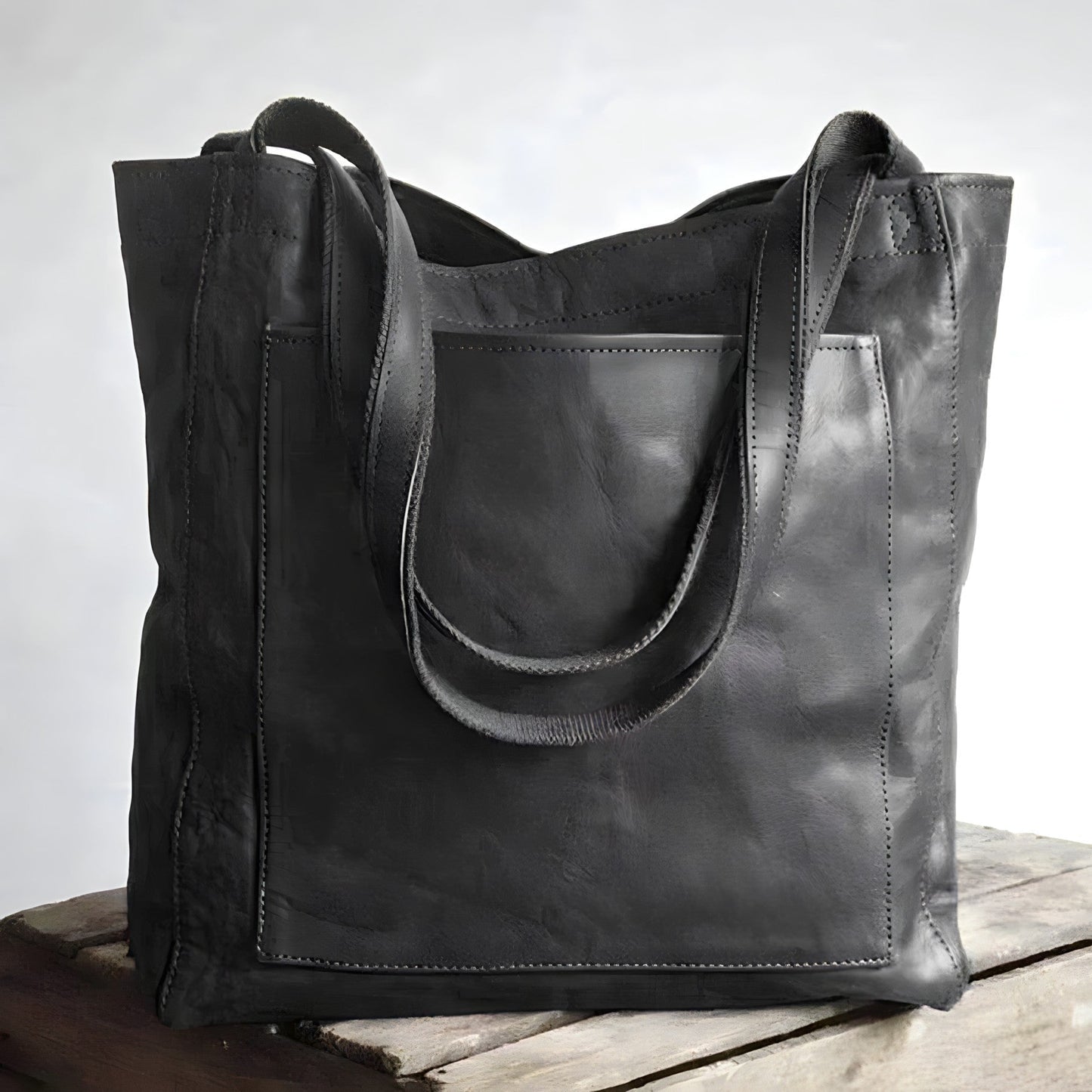Schwarze Ledertasche mit Tragegriffen auf Holztisch, modisch und geräumig.