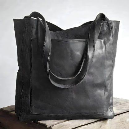 Schwarze Ledertasche mit Tragegriffen auf Holztisch, modisch und geräumig.