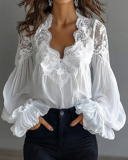 Weiße Bluse mit Spitzenausschnitt und Rüschenmanschetten, getragen von einem Model mit Händen in den Hosentaschen 1