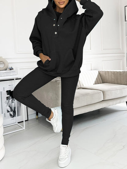 Frau in schwarzem Jumpsuit und weißen Sneakers in modernem Wohnzimmer.